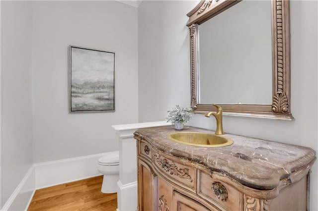 bathroom with baseboards, toilet, wood finished floors, and vanity