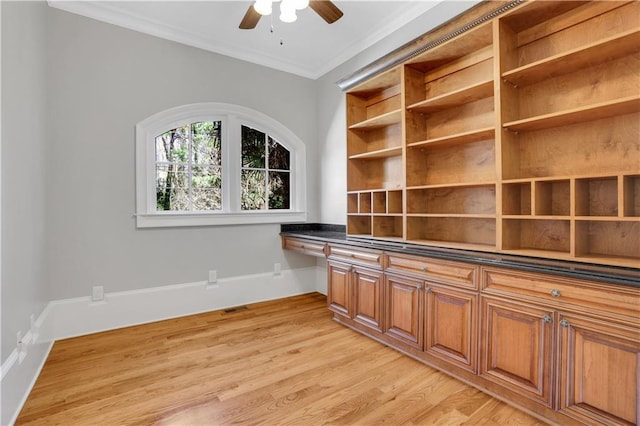 unfurnished office with a ceiling fan, baseboards, light wood-style floors, built in desk, and crown molding