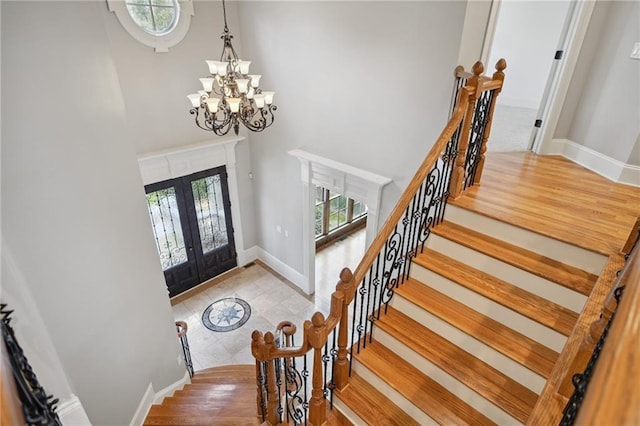entryway featuring wood finished floors, french doors, a high ceiling, an inviting chandelier, and baseboards