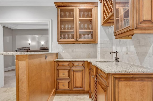 kitchen featuring brown cabinets, a sink, light stone counters, glass insert cabinets, and decorative backsplash