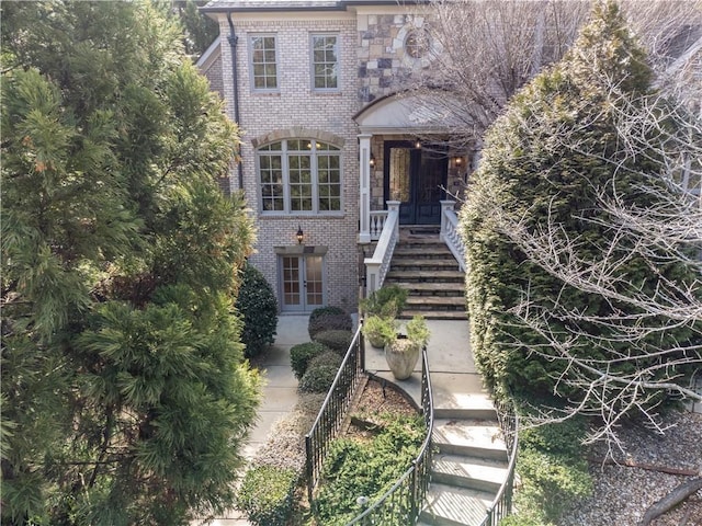 view of front of house featuring french doors, brick siding, and stairway