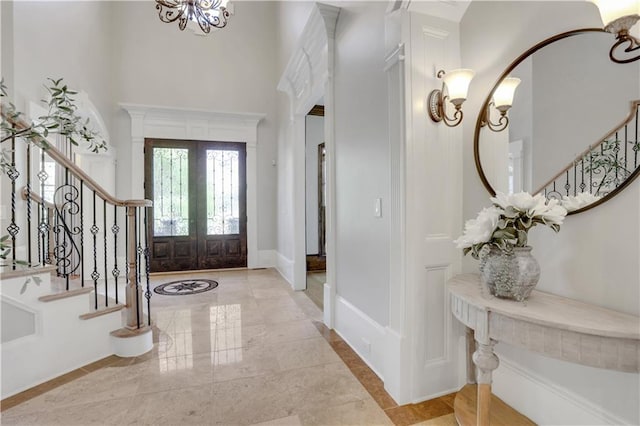 foyer entrance with baseboards, stairs, french doors, a towering ceiling, and a notable chandelier