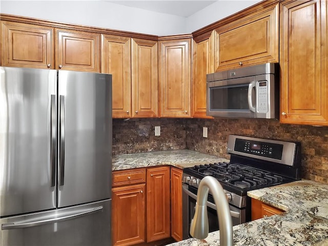 1649 Southgate Mill Dr, Duluth, GA 30096 - kitchen featuring appliances with stainless steel finishes, tasteful backsplash, light stone counters, and brown cabinetry