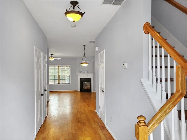 hall with stairs, light wood-type flooring, visible vents, and baseboards