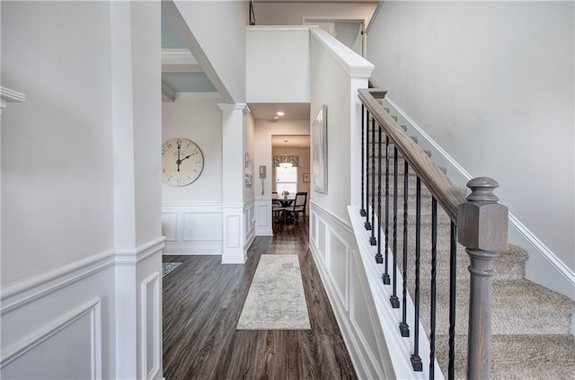 foyer entrance with dark wood-type flooring, stairway, wainscoting, a decorative wall, and decorative columns