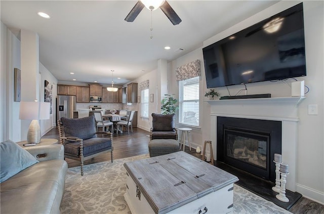 living room with light wood-type flooring, a glass covered fireplace, recessed lighting, baseboards, and ceiling fan