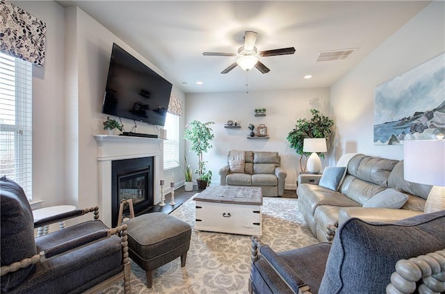 living area with wood finished floors, baseboards, visible vents, a ceiling fan, and a glass covered fireplace