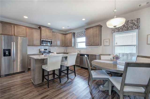 kitchen with visible vents, a kitchen island, dark wood finished floors, a breakfast bar, and appliances with stainless steel finishes