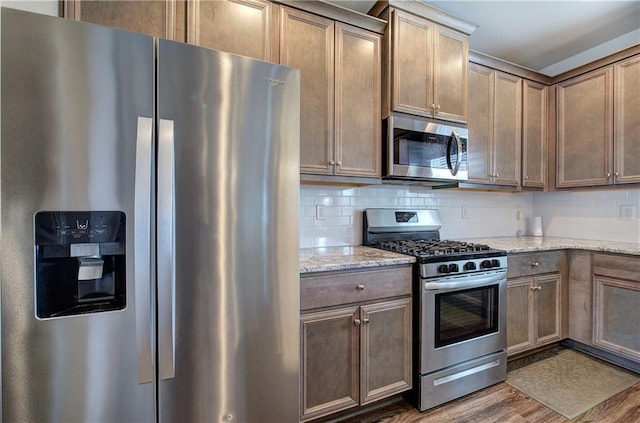 kitchen with stainless steel appliances, light stone countertops, wood finished floors, and decorative backsplash