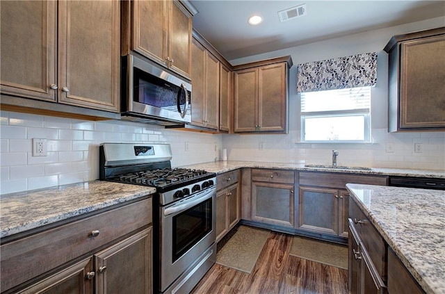 kitchen with tasteful backsplash, visible vents, dark wood-type flooring, stainless steel appliances, and a sink