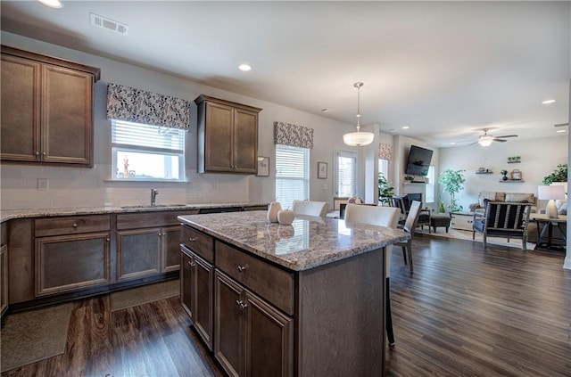 kitchen featuring visible vents, dark wood-type flooring, a sink, open floor plan, and a center island