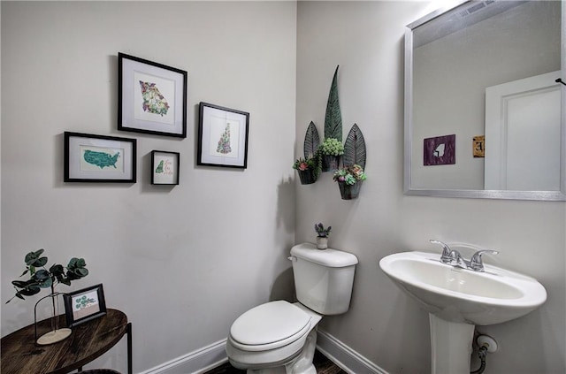 half bathroom featuring toilet, visible vents, baseboards, and a sink