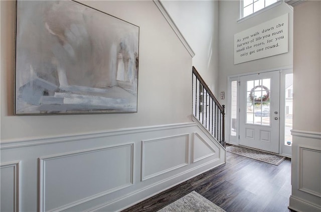 foyer entrance featuring dark wood-style floors, stairway, a decorative wall, and a wainscoted wall