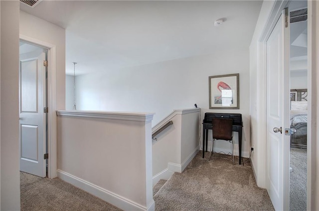 hallway with an upstairs landing, visible vents, baseboards, and carpet