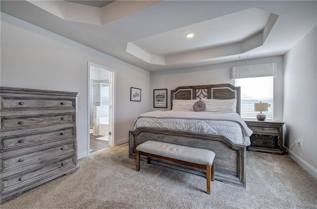 carpeted bedroom with baseboards, a raised ceiling, and ensuite bath