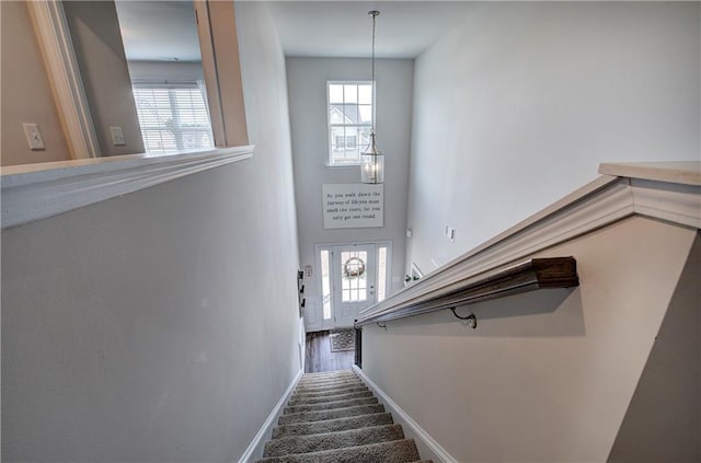 staircase featuring a chandelier, a healthy amount of sunlight, a high ceiling, and baseboards