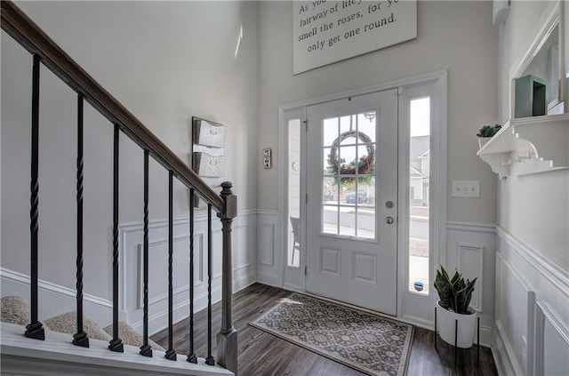 entrance foyer featuring stairway, dark wood-type flooring, wainscoting, and a decorative wall