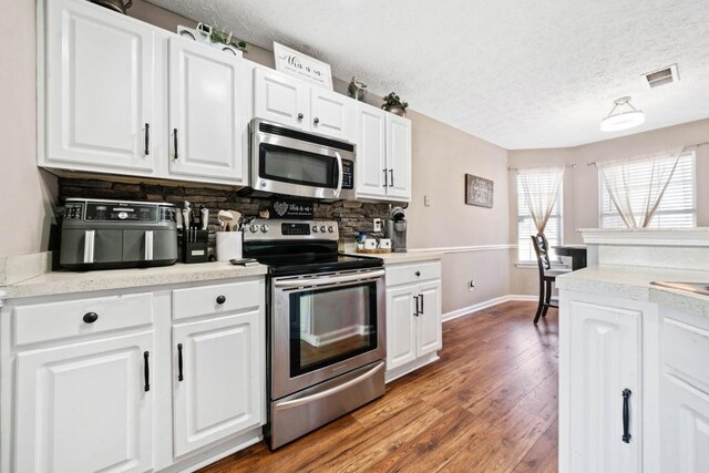 565 Saint James Ct, Lawrenceville, GA 30044 - kitchen with appliances with stainless steel finishes, tasteful backsplash, white cabinetry, wood-type flooring, and a textured ceiling