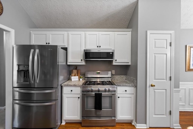 kitchen featuring appliances with stainless steel finishes, white cabinets, a textured ceiling, and light stone counters