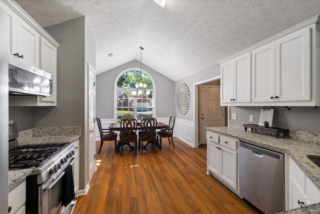 kitchen with dark wood-type flooring, stainless steel appliances, vaulted ceiling, white cabinets, and light stone counters