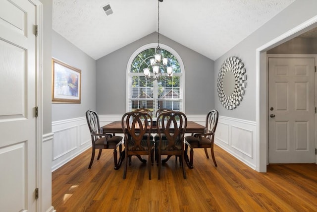 dining area featuring vaulted ceiling, a textured ceiling, dark hardwood / wood-style flooring, and an inviting chandelier