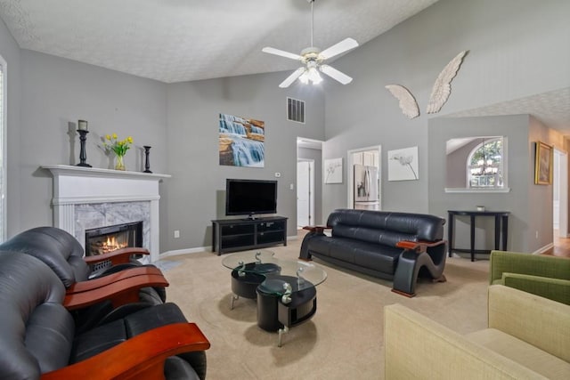 living room with light carpet, a high end fireplace, a textured ceiling, high vaulted ceiling, and ceiling fan