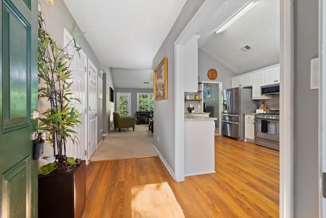 interior space featuring white cabinetry, light hardwood / wood-style floors, appliances with stainless steel finishes, and vaulted ceiling