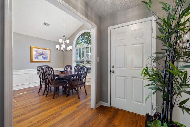 dining room with an inviting chandelier, lofted ceiling, a textured ceiling, and dark wood-type flooring