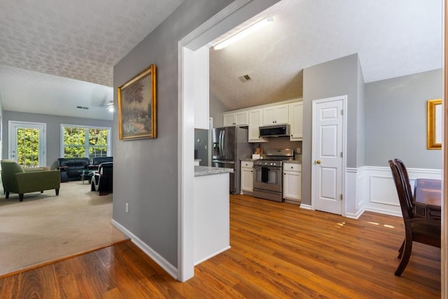 kitchen with appliances with stainless steel finishes, a textured ceiling, hardwood / wood-style floors, white cabinetry, and vaulted ceiling