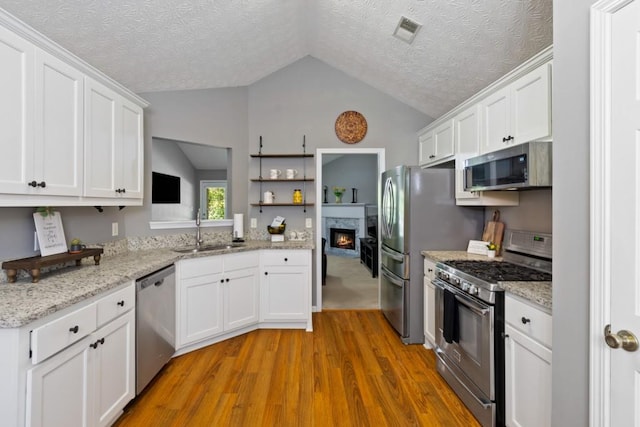 kitchen with stainless steel appliances, lofted ceiling, sink, and white cabinets