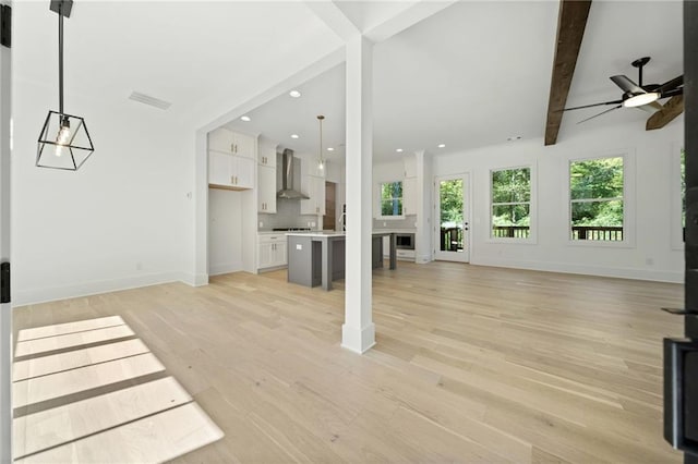 unfurnished living room with ceiling fan, beamed ceiling, and light wood-type flooring