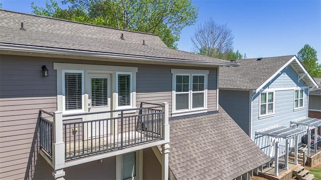 rear view of house featuring roof with shingles and a balcony