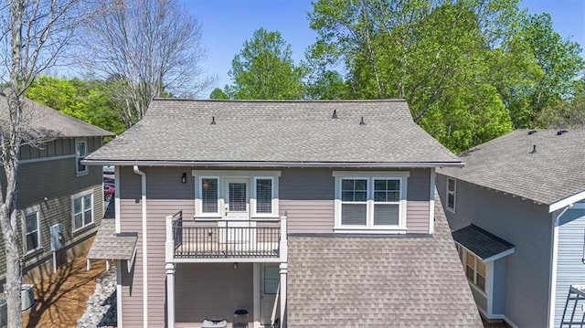 rear view of house featuring a shingled roof and a balcony