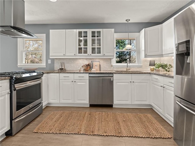 kitchen with island exhaust hood, a sink, appliances with stainless steel finishes, white cabinets, and stone counters