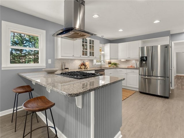 kitchen featuring a peninsula, island exhaust hood, a sink, stainless steel appliances, and white cabinets