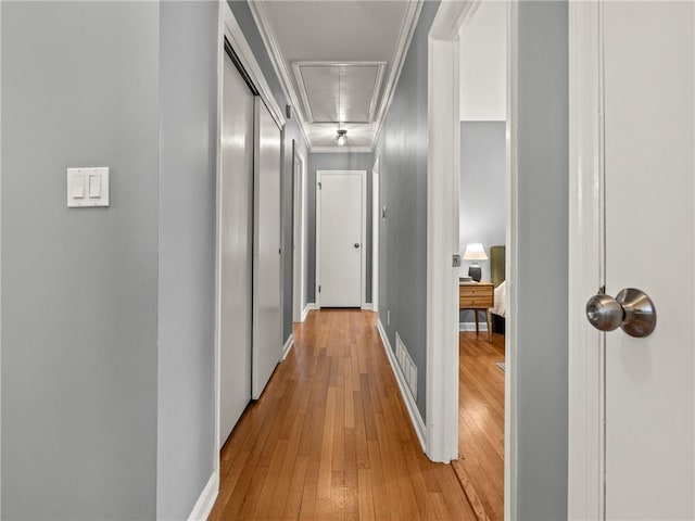 hall with visible vents, ornamental molding, light wood finished floors, baseboards, and attic access