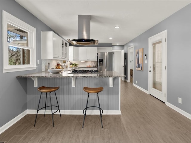 kitchen with light stone counters, a peninsula, appliances with stainless steel finishes, tasteful backsplash, and island range hood