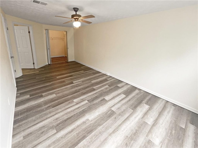 unfurnished bedroom with wood-type flooring, a closet, ceiling fan, and a spacious closet