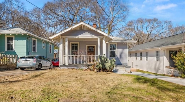 bungalow-style home featuring a porch, a chimney, and a front lawn