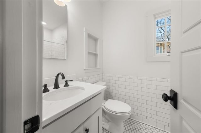 bathroom featuring toilet, a wainscoted wall, a tile shower, vanity, and tile walls