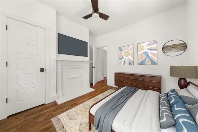 bedroom featuring a ceiling fan, a fireplace with flush hearth, dark wood finished floors, and baseboards