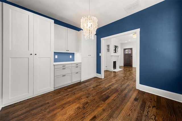 unfurnished dining area with baseboards, a fireplace with flush hearth, dark wood finished floors, and a notable chandelier