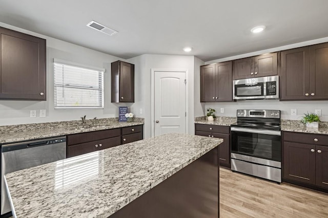 kitchen with sink, dark brown cabinets, light hardwood / wood-style flooring, stainless steel appliances, and light stone countertops