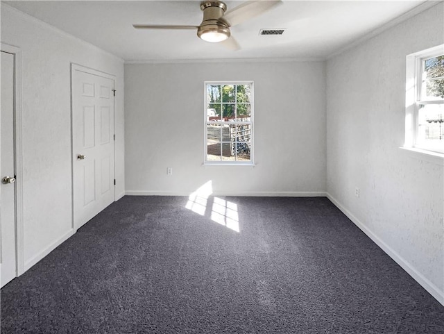 spare room with dark colored carpet, ceiling fan, ornamental molding, and a wealth of natural light