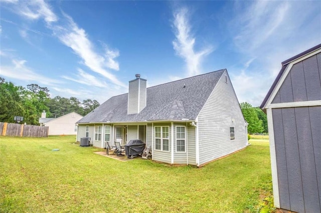 back of property featuring a shingled roof, a yard, central AC, a chimney, and fence