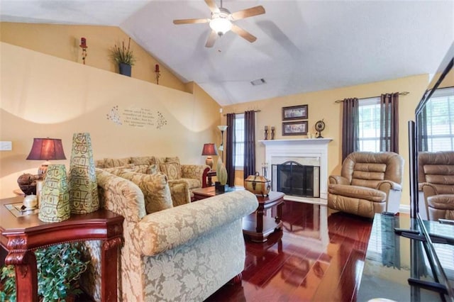 living room featuring wood finished floors, a fireplace with raised hearth, visible vents, a ceiling fan, and high vaulted ceiling