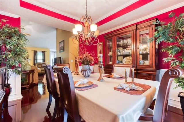 dining room featuring wood finished floors, an inviting chandelier, ornamental molding, and a raised ceiling