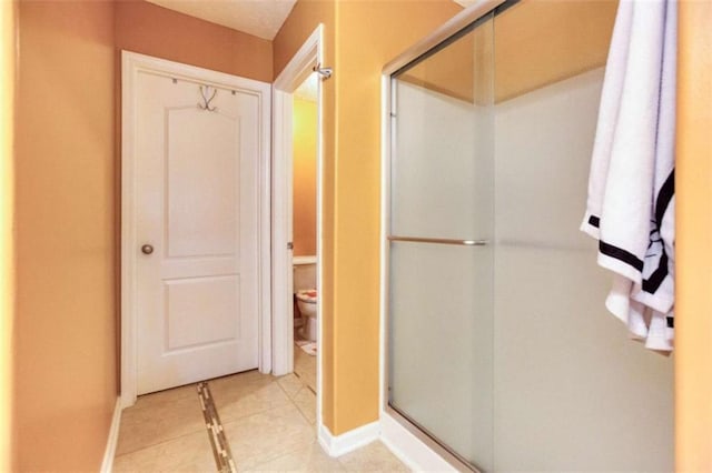 bathroom with toilet, a shower stall, tile patterned floors, and baseboards