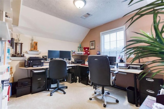 home office with a textured ceiling, visible vents, vaulted ceiling, and light carpet
