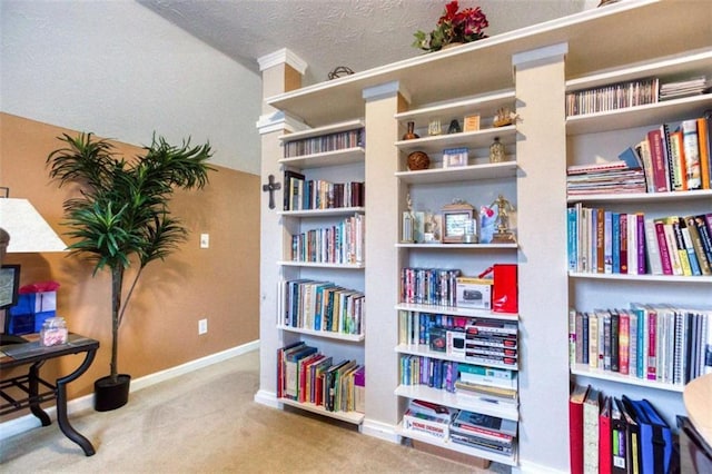 living area with wall of books, baseboards, and carpet floors
